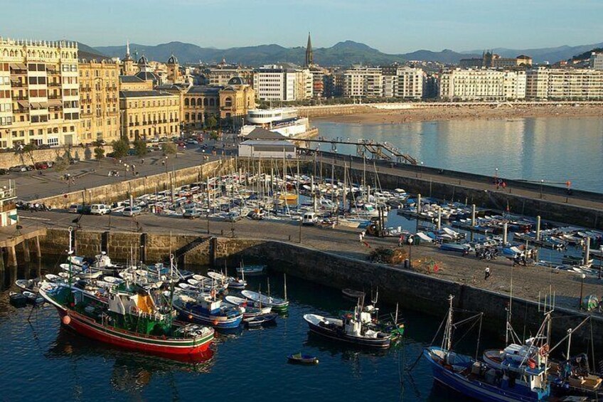 A harbor with boats docked, a large building with a tower, and a cityscape in the background. 2