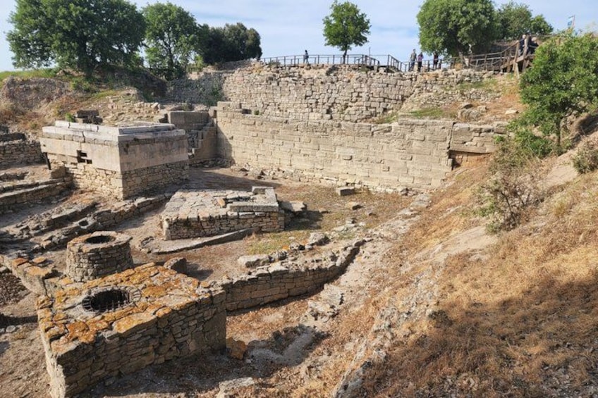 Ruinas antiguas con estructuras y muros de piedra, rodeadas de hierba seca y árboles. 3