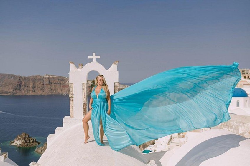 Una mujer con un vestido azul parada sobre un acantilado blanco con una iglesia al fondo. 3