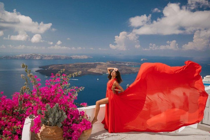 Una mujer con un vestido rojo sentada en un balcón con vista al mar y acantilados. 2