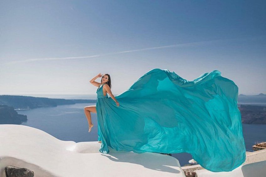 Una persona vestida con un vestido turquesa vaporoso sentada sobre una estructura blanca, con vistas a una masa de agua y tierra lejana. 5