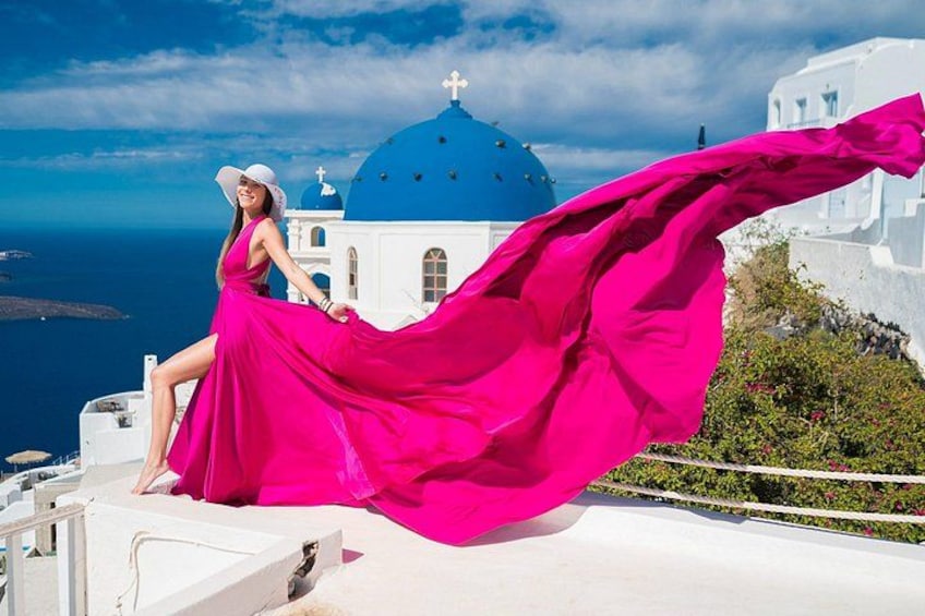 Eine Person in einem pinken Kleid steht vor einem weißen Gebäude mit einer blauen Kuppel und blickt auf das Meer. 5