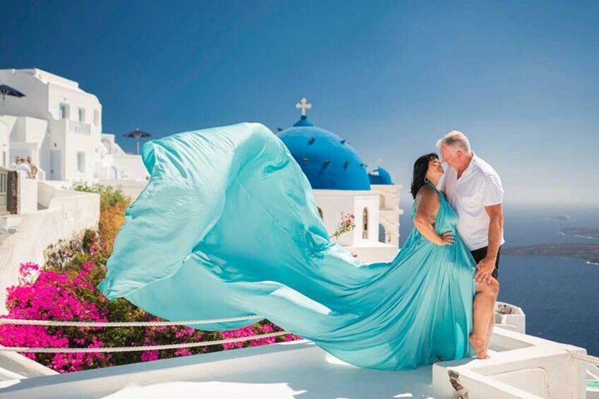 A couple embracing on a rooftop with a view of a blue-domed church and the sea. 2