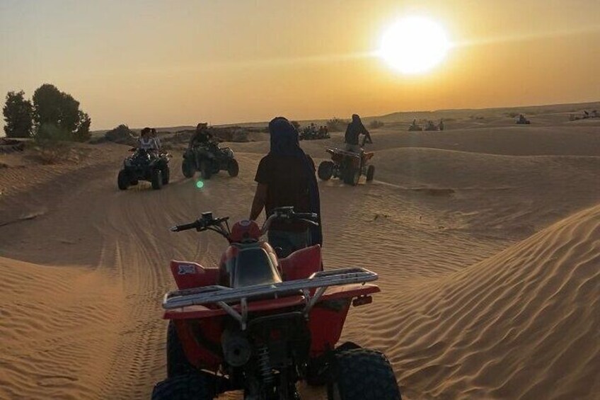 A group of people riding ATVs on a sandy path during sunset. 5
