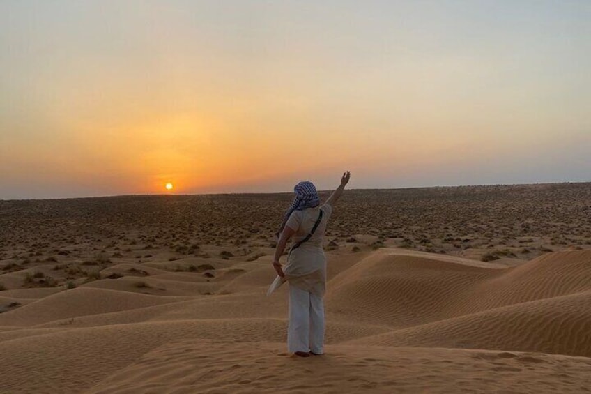 A person standing on sand dunes facing the sunset. 4