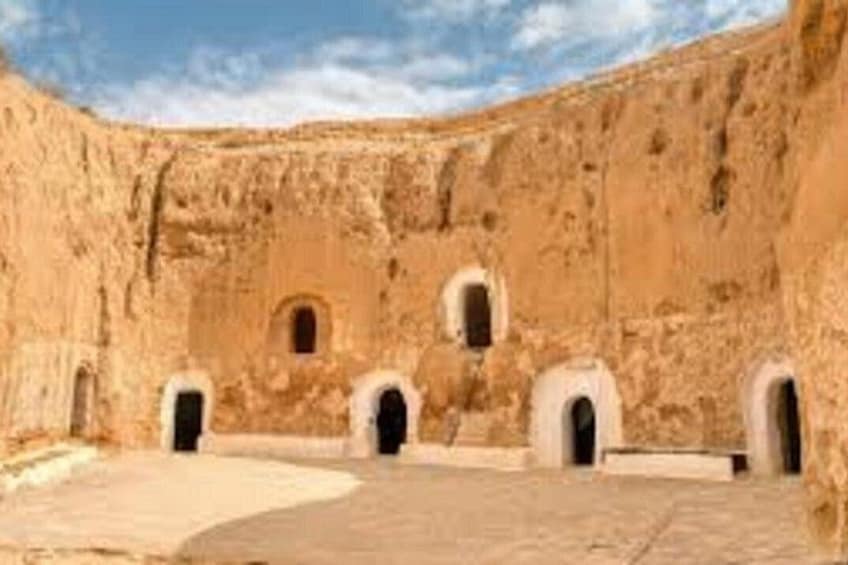 A courtyard with a curved wall, several arched doorways, and a clear sky. 3