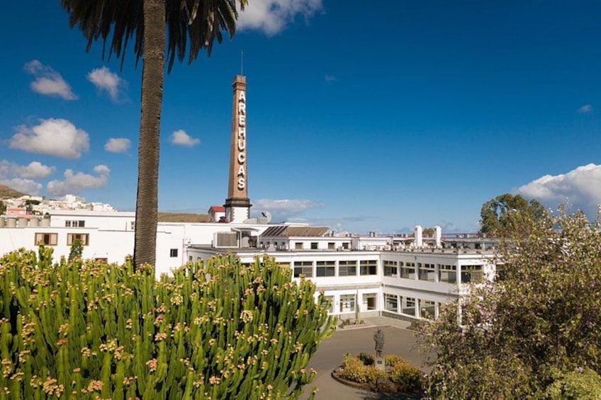 A building with a tall chimney, surrounded by greenery and a clear blue sky. 2