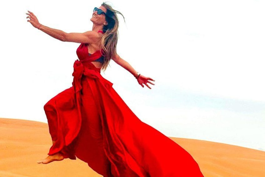 A person in a red dress running through a desert with sand dunes. 2
