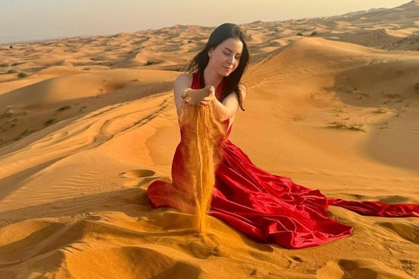 A person in a red dress sitting on sand dunes in a desert landscape. 4