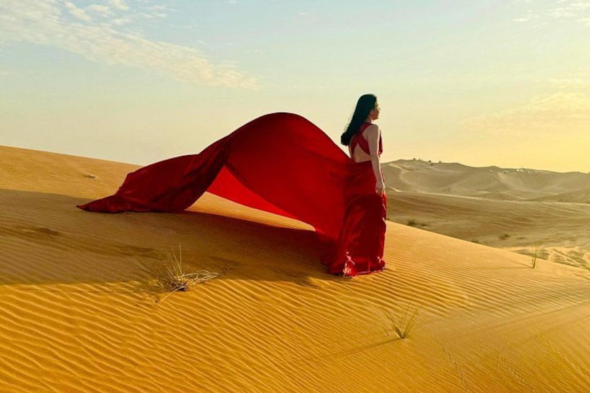 A person in a red dress standing on a sand dune with a vast desert landscape in the background. 1