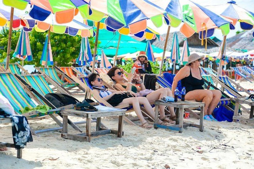 Beach chairs under colorful umbrellas, people relaxing, and a sandy beach. 5