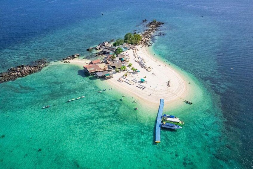 An aerial view of a tropical island with clear turquoise waters, a sandy beach, and a small settlement with buildings and boats. 1
