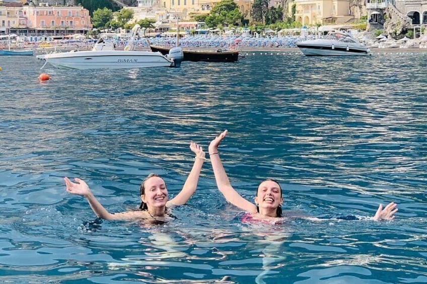 Two people swimming in a body of water with boats and buildings in the background. 3