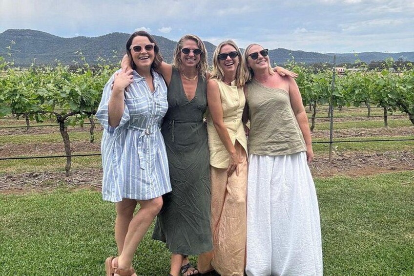 A group of people standing in a vineyard with rows of grapevines and hills in the background. 4