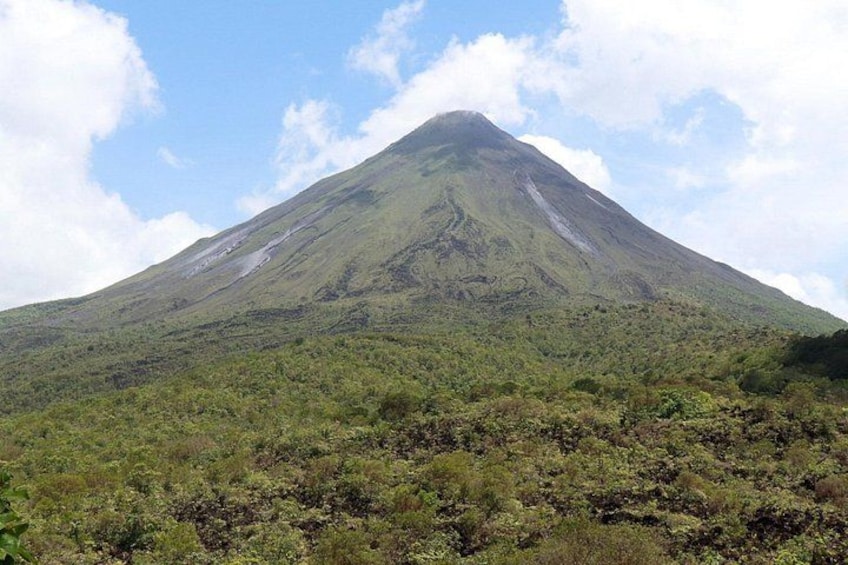 A mountain with a conical shape, dense green vegetation at its base, and a clear sky. 2