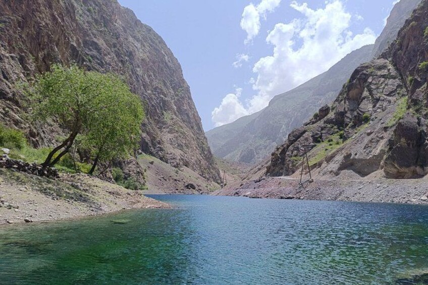 A narrow canyon with a clear blue river, rocky cliffs, and sparse vegetation. 2