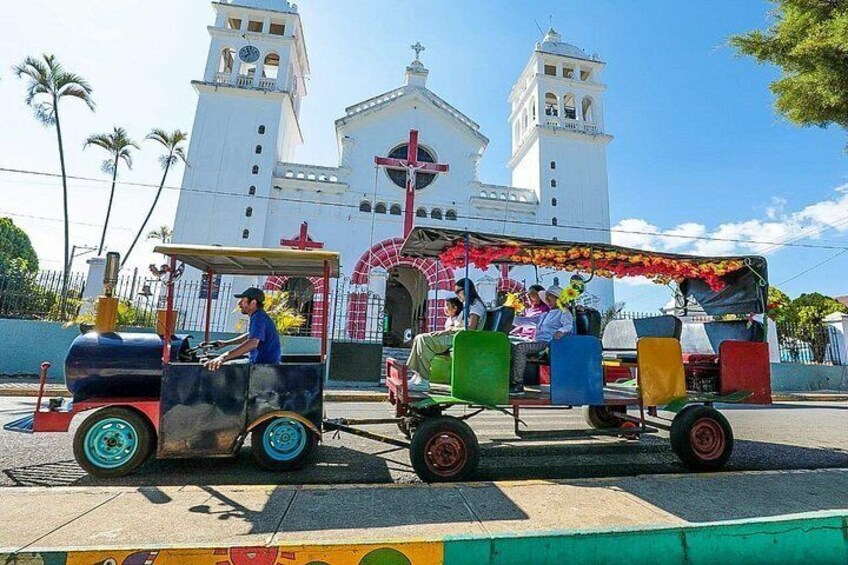 A colorful train with passengers, a church with two towers, and palm trees in the background. 5