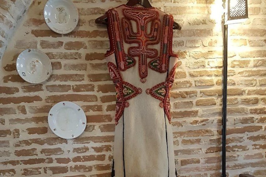 A traditional embroidered garment hanging on a brick wall with plates and a floor lamp. 2