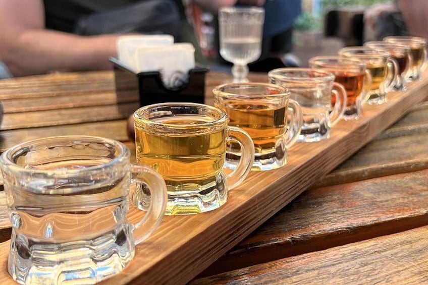 A wooden tray with several clear glass mugs filled with amber liquid, likely tea, on a wooden table. 1