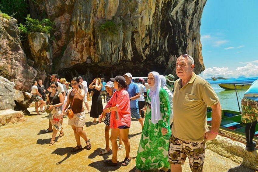 A group of people walking on a rocky beach with a large cave formation in the background. 3