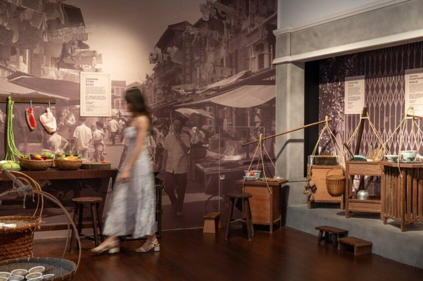 Una exposición histórica con puestos de mercado antiguos, una mujer con vestido y un mural de una calle animada. 2