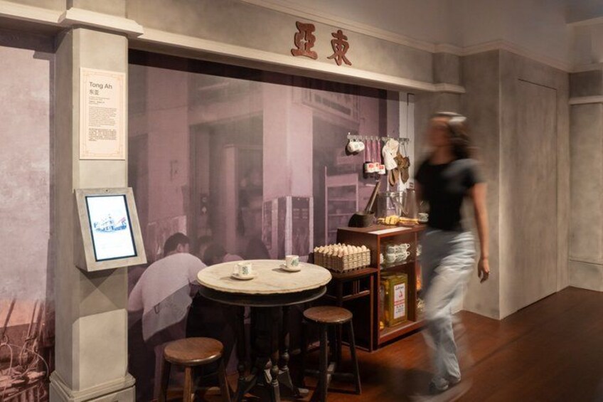 Interior de una tienda tradicional de té, con una mesa redonda, taburetes y estanterías llenas de productos de té. 3