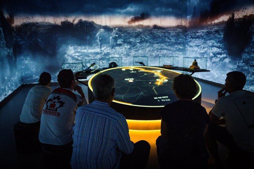 A group of people observing a large circular display with a map and a person standing on a platform. 3