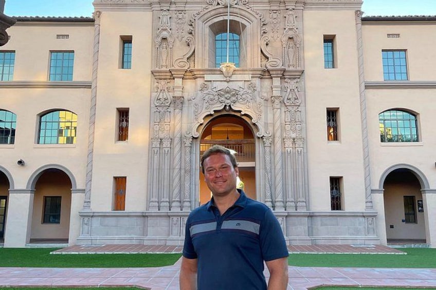 A man standing in front of a building with ornate architectural details and arched windows. 3