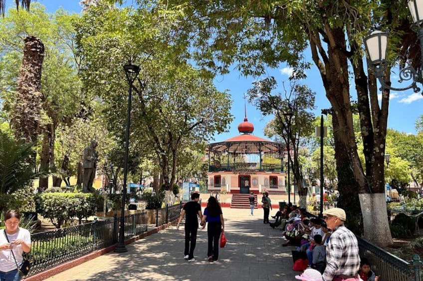 Un parque con un quiosco, árboles y una estatua. 1