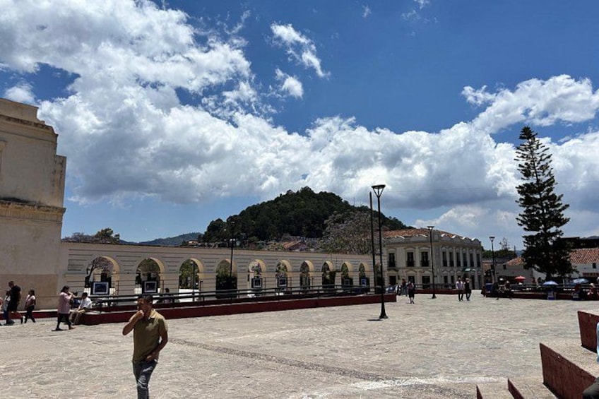 Una plaza con un edificio de ventanas arqueadas y una colina al fondo. 2