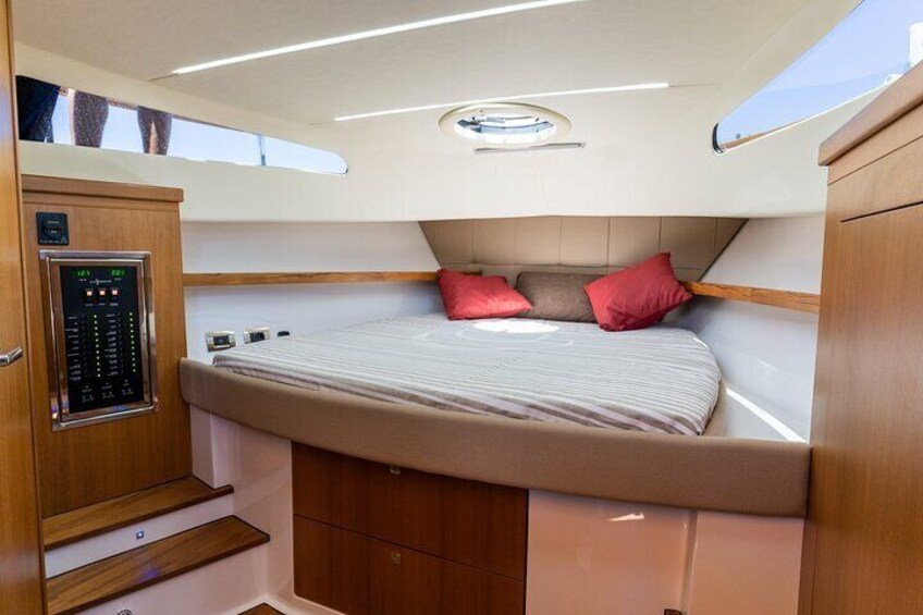 Een compact, goed verlicht interieur met een bed, bedieningspaneel en opbergvakken. 5
