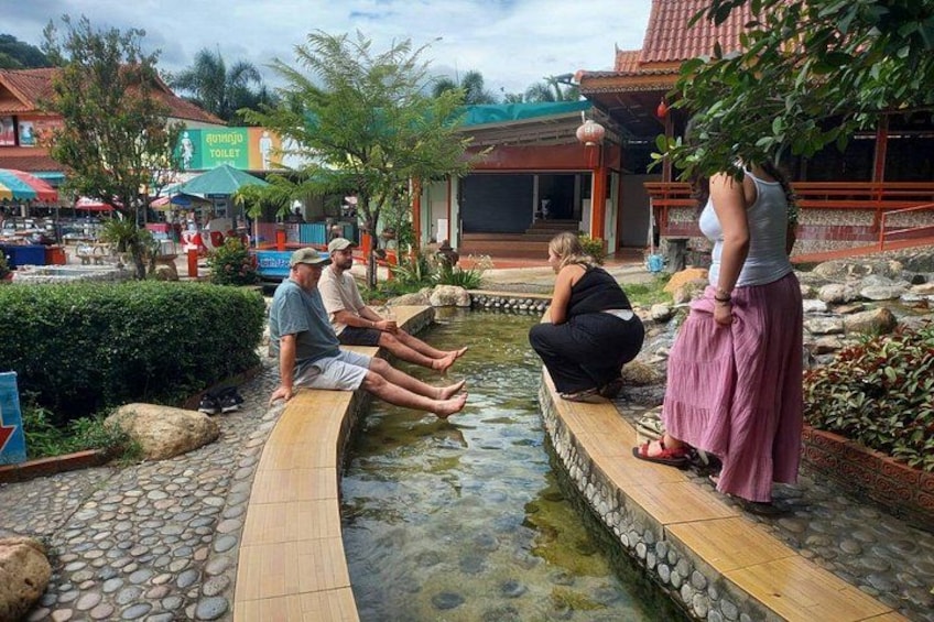 Un groupe de personnes se détend près d’un élément décoratif aquatique, dans un cadre traditionnel agrémenté de chemins de pierre et d’une structure à toit de tuiles. 3