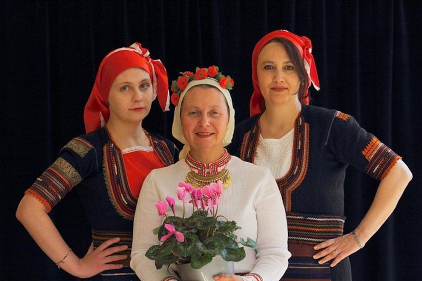 Three people in traditional attire with floral decorations, standing against a dark background. 5