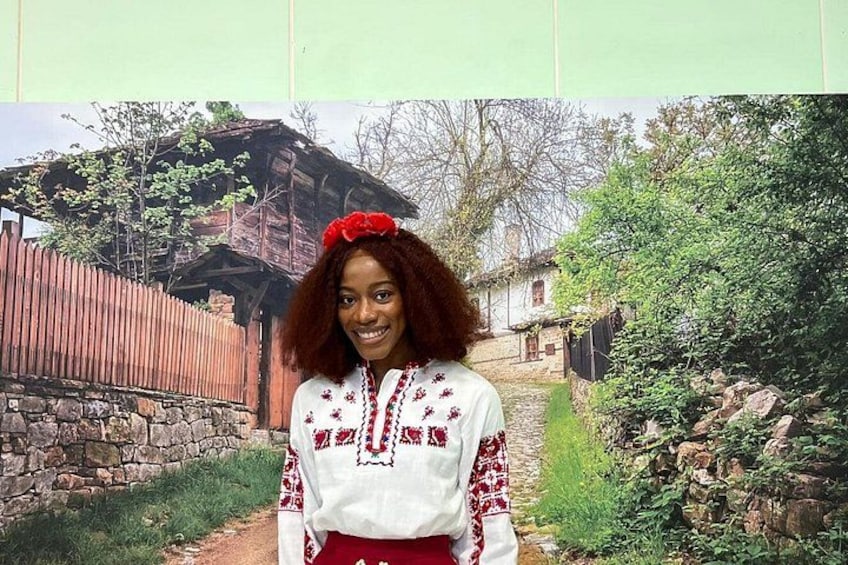 A person in traditional attire standing in front of a rustic building with a stone wall and a wooden fence. 3