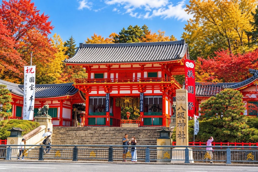 Perinteinen japanilainen temppeli, jossa on punaiset ja valkoiset seinät, laattakatto ja kivestä veistetty patsas edessä. 4