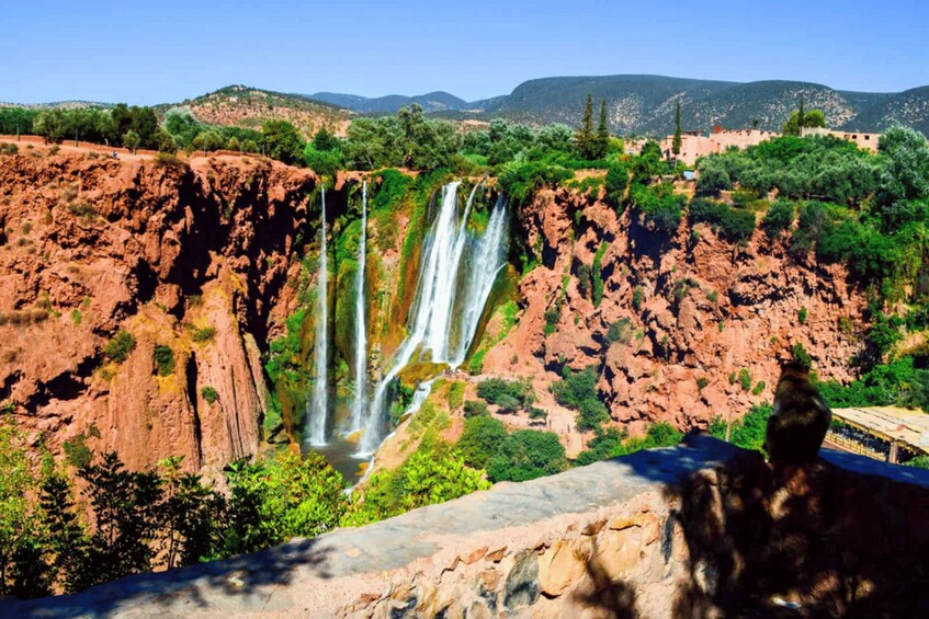 A multi-tiered waterfall cascading down a rocky cliff surrounded by lush greenery and distant hills. 3