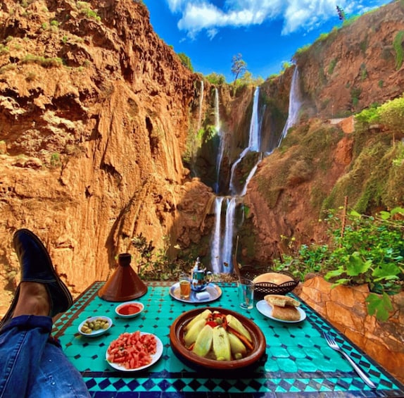 A table with food and a person sitting with a view of a waterfall. 2
