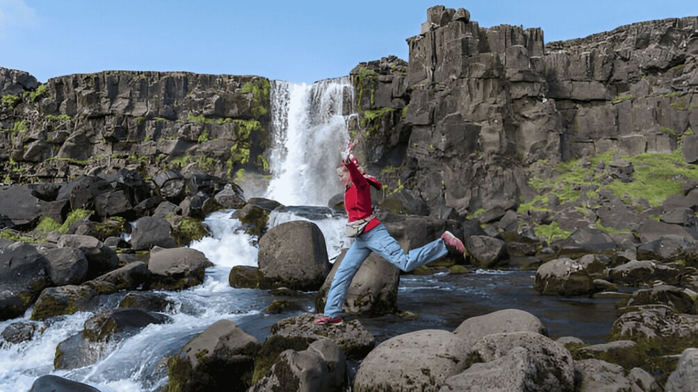 A person jumping in front of a waterfall with a rocky landscape in the background. 3