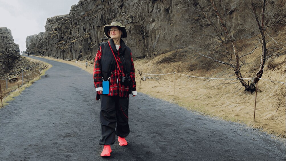 A person walking on a paved path surrounded by rocky cliffs and sparse vegetation. 5