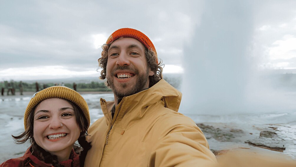 Two people wearing winter hats and jackets, standing on a snowy beach with a cloudy sky. 2