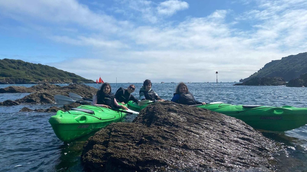 A group of people kayaking on a calm sea with rocky shores and a sailboat in the distance. 3