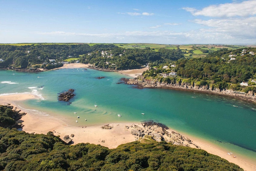A coastal landscape with a sandy beach, clear turquoise waters, and surrounding green hills. 2