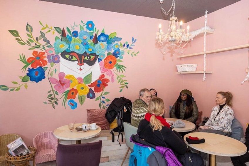 Un grupo de personas sentadas alrededor de una mesa en una habitación con un mural de un gato rodeado de flores. 4
