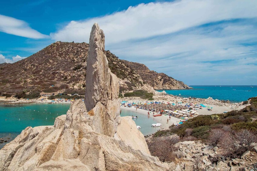 A coastal landscape with a prominent rock formation, a beach with umbrellas and people, and a mountain in the background. 1