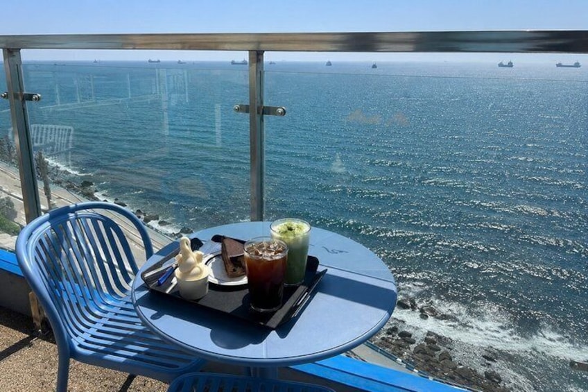A table with drinks and a cake on a balcony overlooking the ocean. 3