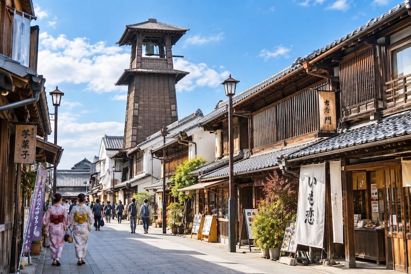 A traditional Japanese street with wooden buildings, a bell tower, and pedestrians. 4