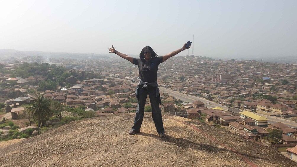 A person standing on a hill with arms raised, overlooking a cityscape with numerous buildings and a prominent tower. 3