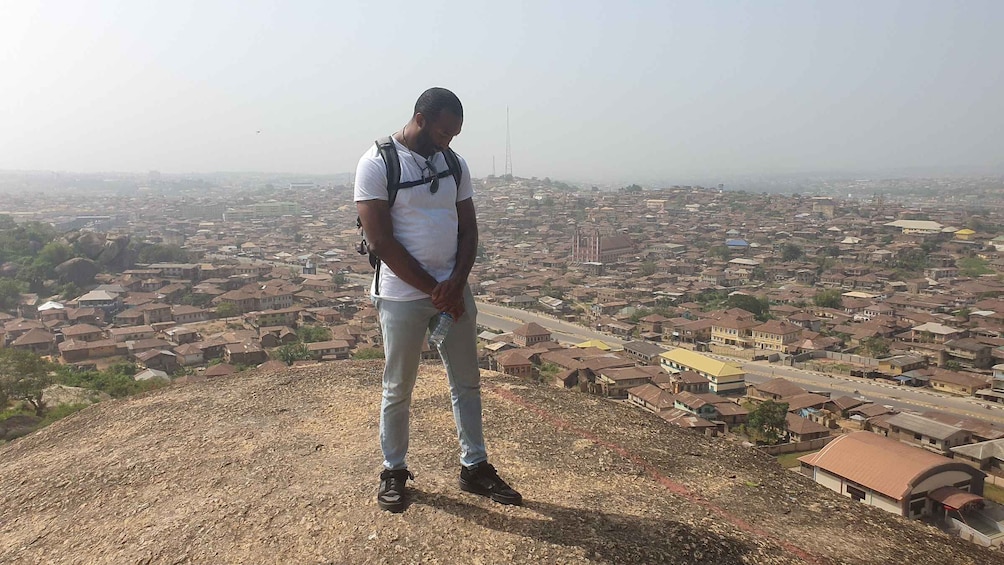 A man standing on a hill overlooking a cityscape with numerous buildings and a tall tower in the distance. 3