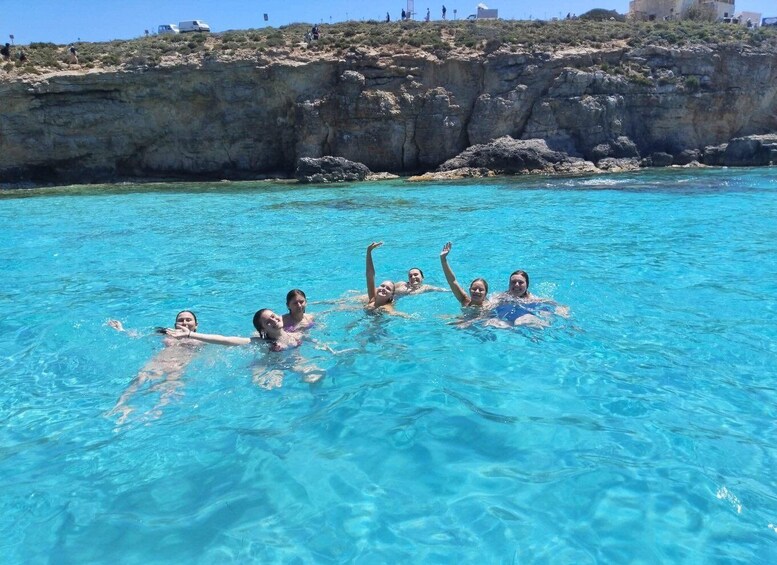 A group of people swimming in a clear blue pool with rocky cliffs in the background. 4