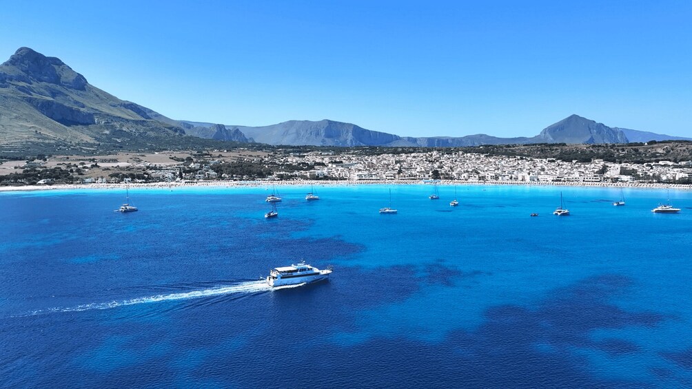 A coastal town with a clear blue sea, boats, and mountains in the background. 3